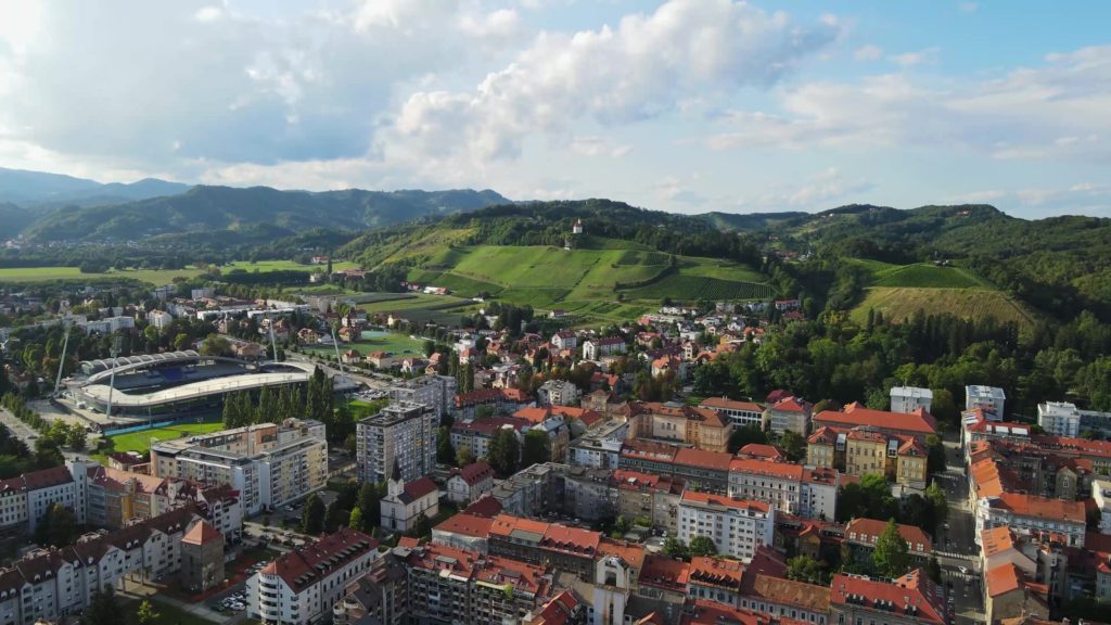 Widok na drona na obrzeża Mariboru, zabudowania, park i góry w oddali