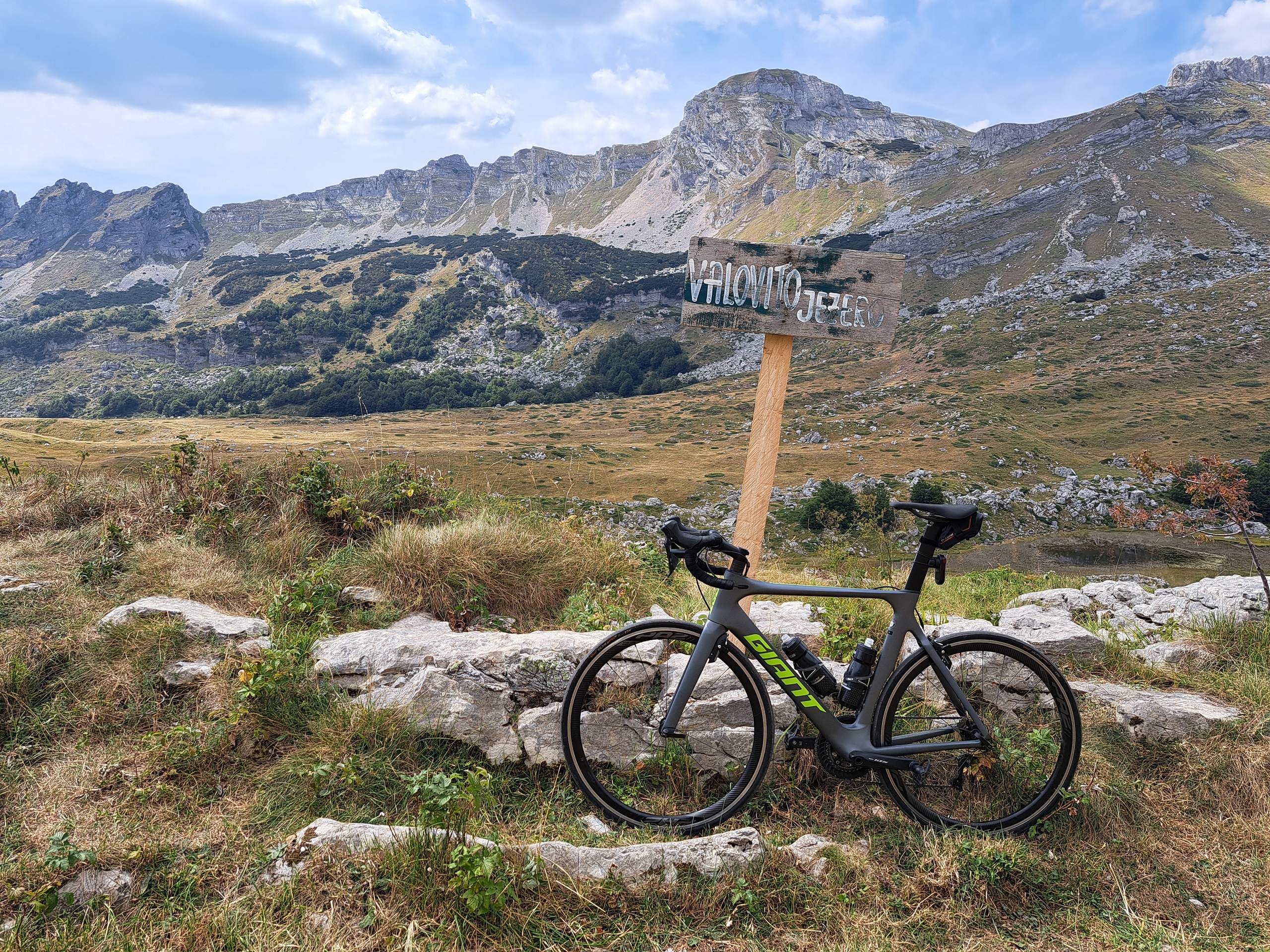 Czarnogóra na rowerze - zdjęcie wykonane w Parku Narodowym Durmitor. Rower szosowy oparty o tabliczkę z nazwą jeziora, w tle góry.